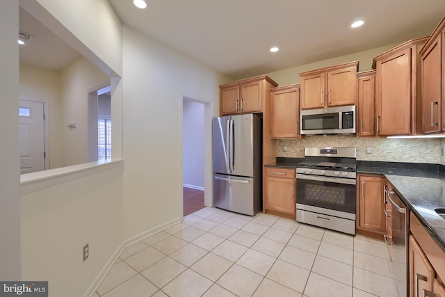 kitchen featuring appliances with stainless steel finishes, tasteful backsplash, dark stone counters, and light tile patterned flooring