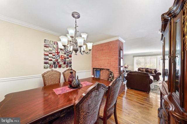 dining space with a fireplace, an inviting chandelier, crown molding, and light hardwood / wood-style flooring