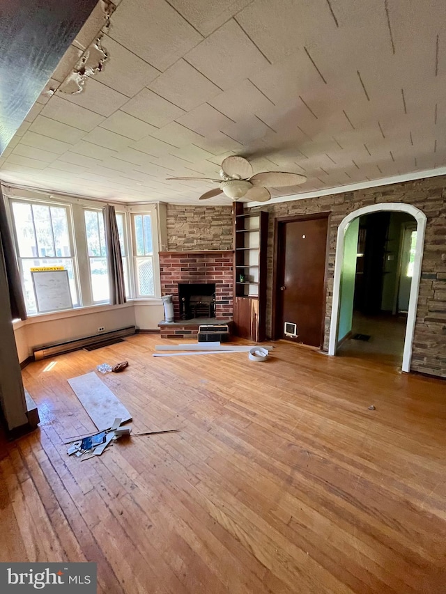 unfurnished living room featuring ceiling fan, a baseboard radiator, built in features, a fireplace, and hardwood / wood-style floors