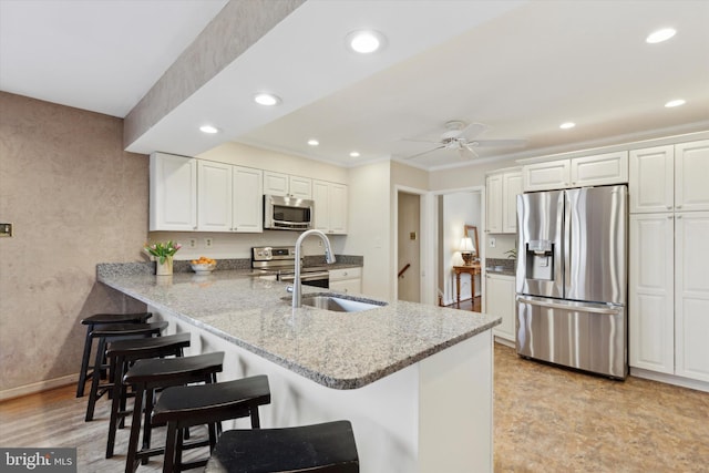 kitchen featuring kitchen peninsula, stainless steel appliances, ceiling fan, and white cabinets