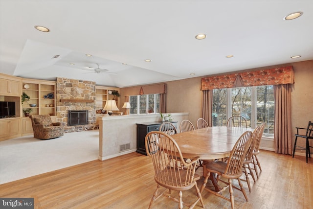 dining space with a fireplace, ceiling fan, built in features, light hardwood / wood-style flooring, and a tray ceiling