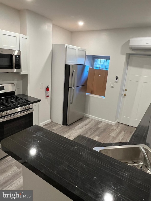 kitchen with white cabinets, a wall mounted air conditioner, light wood-type flooring, and stainless steel appliances