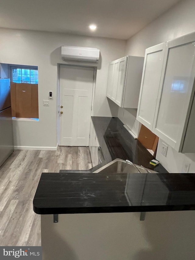 kitchen with kitchen peninsula, light wood-type flooring, white cabinetry, and an AC wall unit