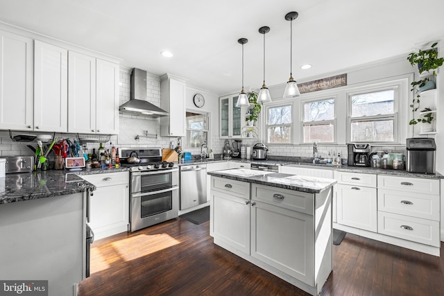 kitchen featuring white cabinets, wall chimney range hood, sink, a kitchen island, and stainless steel appliances