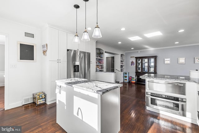 kitchen with light stone countertops, decorative light fixtures, a kitchen island, white cabinetry, and stainless steel appliances