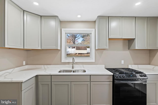 kitchen with gas stove, light stone counters, gray cabinetry, and sink