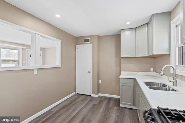 kitchen with light stone counters, gray cabinetry, dark wood-type flooring, sink, and range