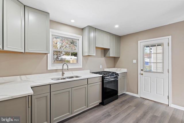 kitchen with light stone countertops, light hardwood / wood-style floors, black range oven, sink, and gray cabinets