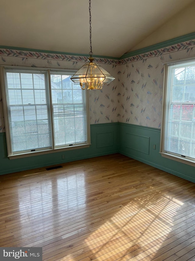 unfurnished dining area featuring plenty of natural light, light hardwood / wood-style floors, vaulted ceiling, and an inviting chandelier