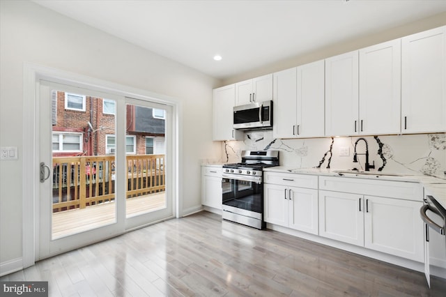 kitchen with light stone counters, stainless steel appliances, white cabinetry, and sink