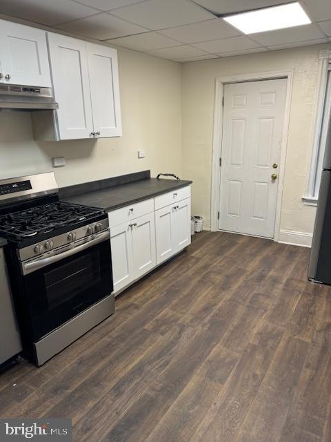 kitchen featuring appliances with stainless steel finishes, a drop ceiling, extractor fan, dark wood-type flooring, and white cabinets