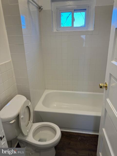 bathroom with hardwood / wood-style floors, toilet, and tiled shower / bath