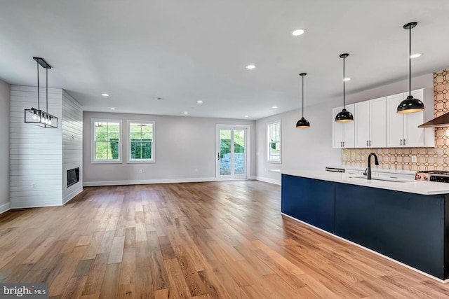 kitchen with light hardwood / wood-style floors, backsplash, a large fireplace, hanging light fixtures, and white cabinets