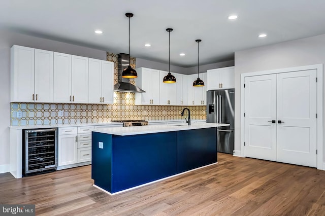 kitchen with white cabinetry, wall chimney range hood, wine cooler, a kitchen island with sink, and high end fridge