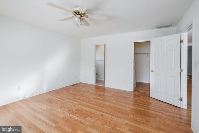 unfurnished bedroom with a closet, a walk in closet, ceiling fan, and light hardwood / wood-style flooring