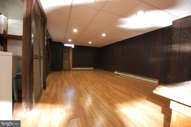 empty room featuring a baseboard radiator, light hardwood / wood-style flooring, and wooden walls