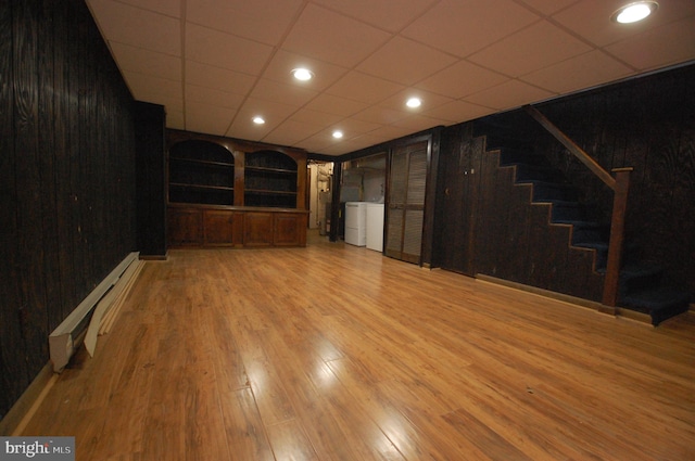 interior space with a baseboard heating unit, light wood-type flooring, wooden walls, and washer / dryer