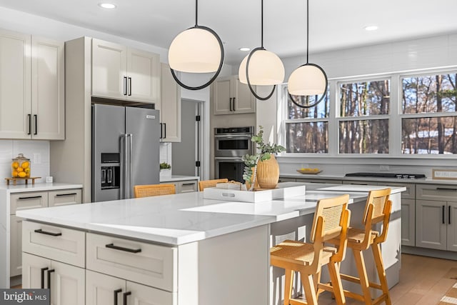 kitchen with light stone countertops, a center island, hanging light fixtures, stainless steel appliances, and decorative backsplash