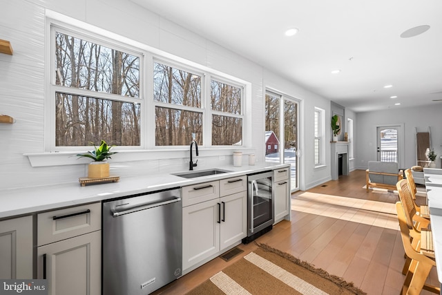 kitchen featuring sink, stainless steel dishwasher, light wood-type flooring, white cabinetry, and beverage cooler