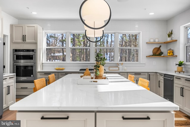 kitchen with gray cabinets, a center island, light stone countertops, and stainless steel double oven