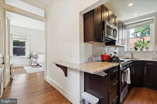 kitchen with a breakfast bar, dark hardwood / wood-style floors, light stone counters, and appliances with stainless steel finishes