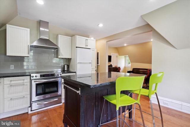 kitchen featuring white cabinetry, wall chimney exhaust hood, a kitchen island, white fridge, and stainless steel stove