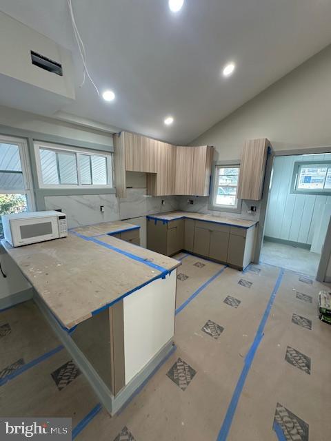 kitchen with kitchen peninsula, light brown cabinets, and vaulted ceiling