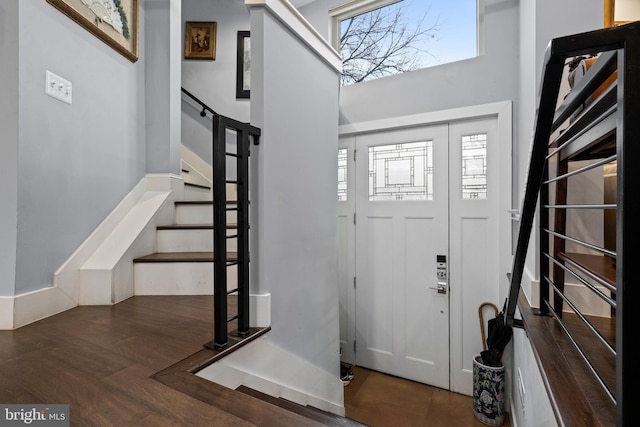 foyer entrance with dark hardwood / wood-style flooring, a towering ceiling, and a healthy amount of sunlight