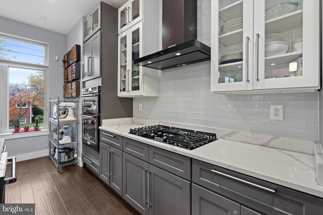 kitchen featuring gray cabinetry, wall chimney exhaust hood, dark hardwood / wood-style floors, gas stovetop, and light stone counters