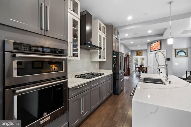 kitchen with gray cabinetry, wall chimney range hood, light stone countertops, tasteful backsplash, and stainless steel appliances