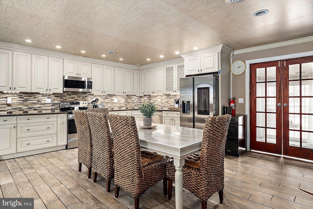 kitchen with stainless steel appliances, decorative backsplash, french doors, crown molding, and white cabinets