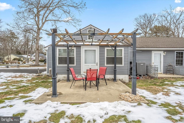 snow covered back of property featuring central AC unit, a pergola, and a patio