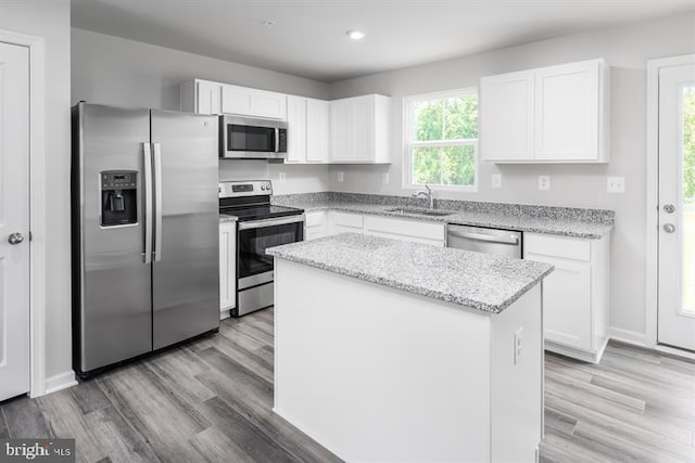 kitchen with white cabinetry, a center island, sink, stainless steel appliances, and light stone counters