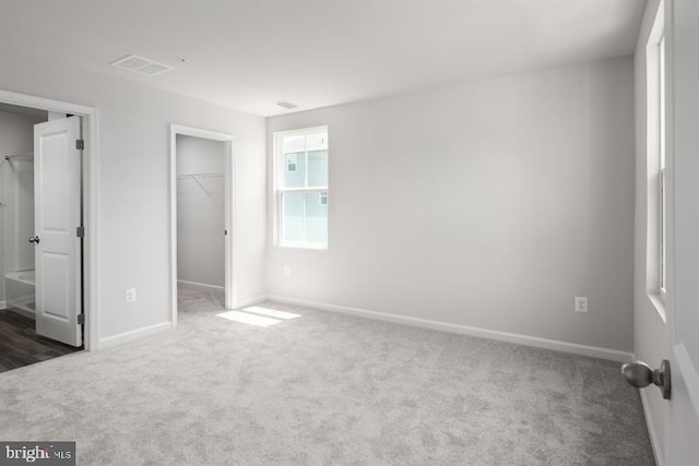 unfurnished bedroom with a walk in closet, a closet, and dark carpet