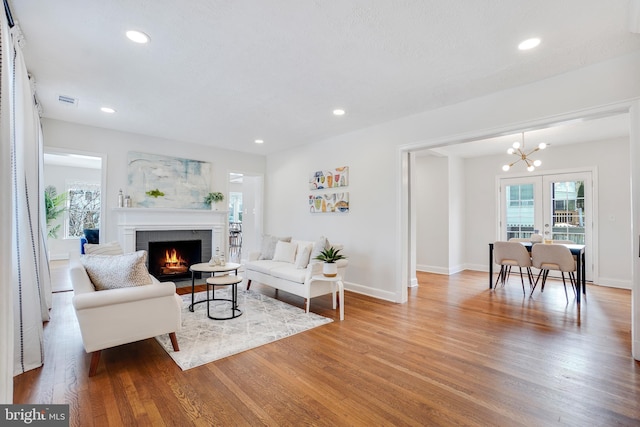 living room featuring a fireplace, a notable chandelier, wood-type flooring, and french doors