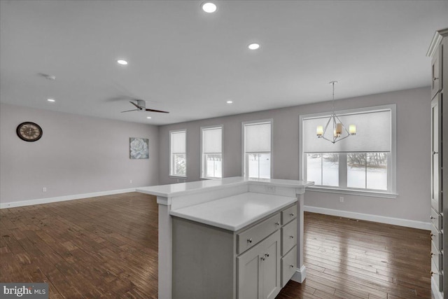 kitchen featuring ceiling fan with notable chandelier, a kitchen island, hanging light fixtures, and dark wood-type flooring