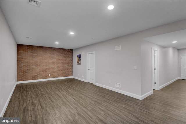 unfurnished room featuring hardwood / wood-style floors and brick wall