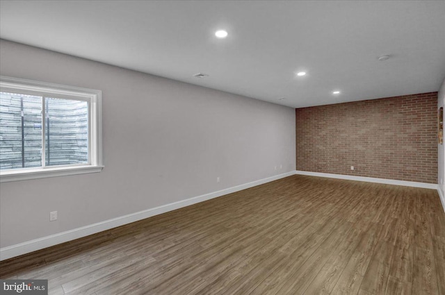 spare room featuring brick wall and light hardwood / wood-style floors