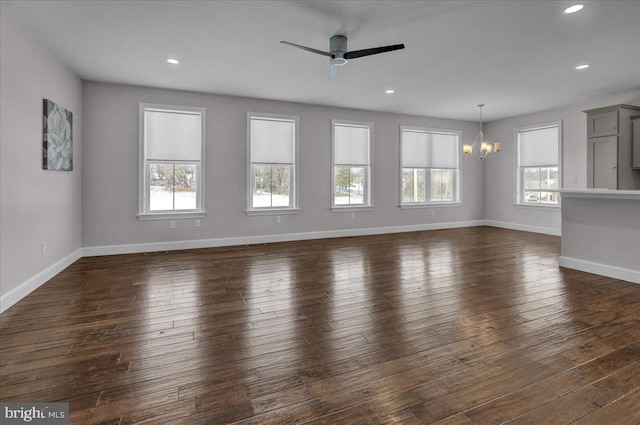 unfurnished living room featuring ceiling fan with notable chandelier, a healthy amount of sunlight, and dark hardwood / wood-style floors