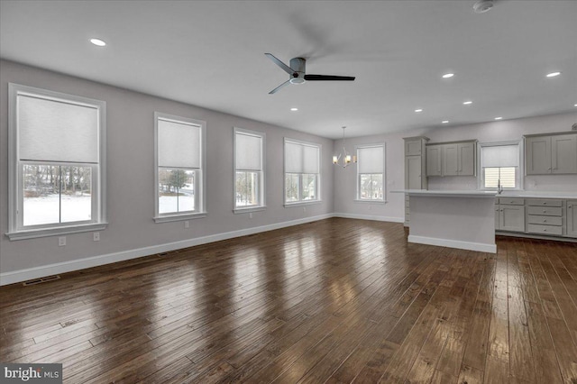 unfurnished living room with ceiling fan with notable chandelier and dark hardwood / wood-style flooring