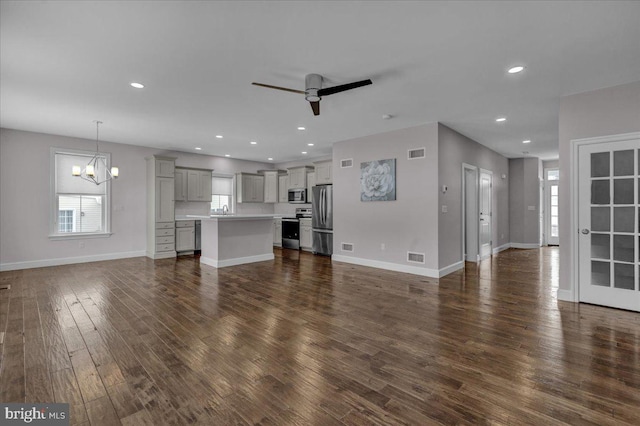 unfurnished living room with ceiling fan with notable chandelier and dark wood-type flooring