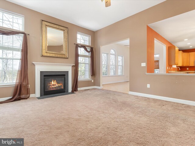 unfurnished living room with ceiling fan, light colored carpet, and plenty of natural light