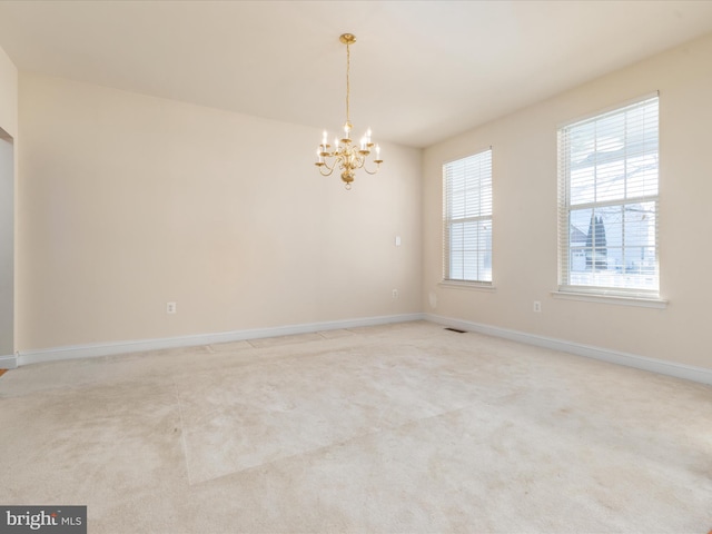 empty room with light colored carpet and a notable chandelier