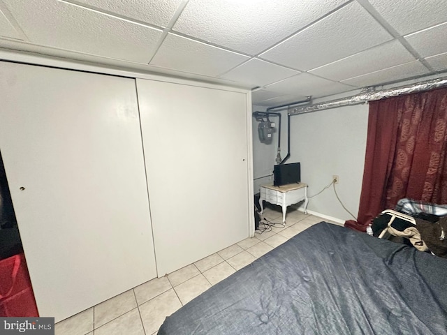 bedroom with light tile patterned floors, a drop ceiling, and a closet