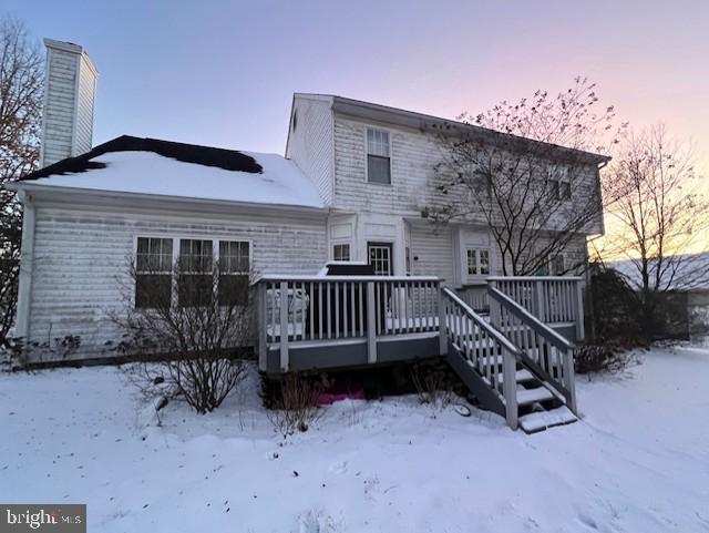 snow covered back of property with a deck