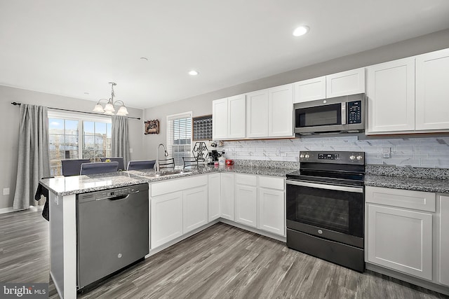 kitchen with a chandelier, kitchen peninsula, stainless steel appliances, and white cabinetry