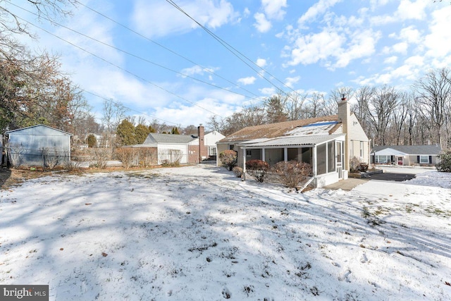 snow covered rear of property with a sunroom