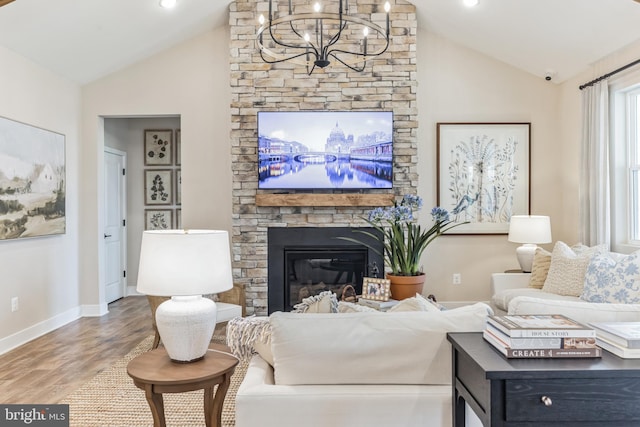 living room featuring an inviting chandelier, hardwood / wood-style flooring, a stone fireplace, and lofted ceiling