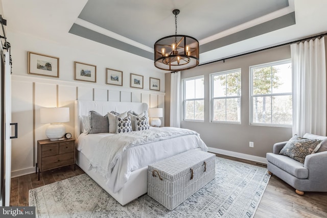 bedroom featuring a tray ceiling, hardwood / wood-style flooring, and an inviting chandelier