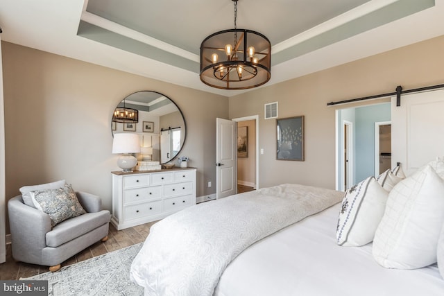 bedroom with a barn door, an inviting chandelier, a raised ceiling, and light hardwood / wood-style floors